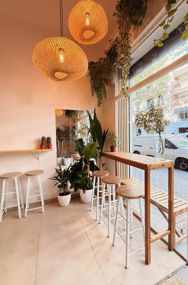 Interior de HOROSCOFFEE con lámparas de ratán, plantas y taburetes de madera junto al ventanal